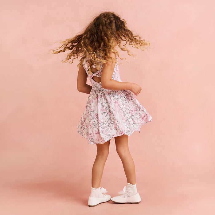 Child twirling in a floral printed dress on a pink bakcground