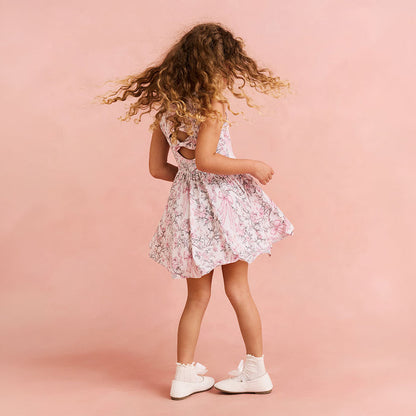 Child twirling in a floral printed dress on a pink bakcground