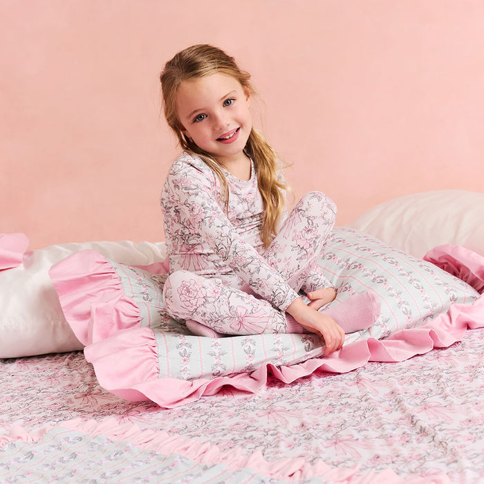 Young girl in a floral pajama set sitting on a bed with pink bedding.