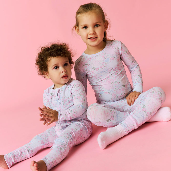 Two children wearing matching floral pajamas on a pink background