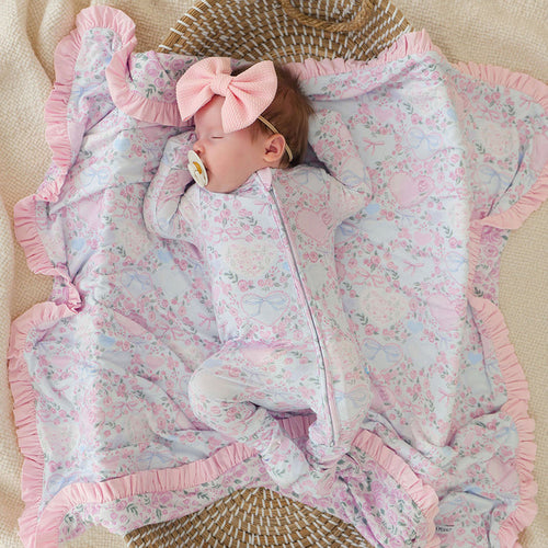 Baby lying on a floral blanket with a pink bow, wearing a matching outfit.