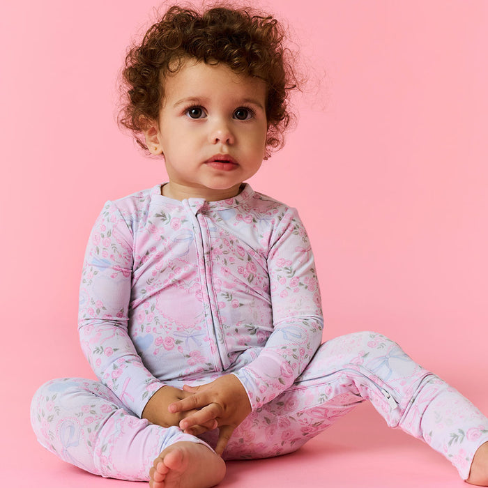 Child wearing a floral pajama one piece on a pink background