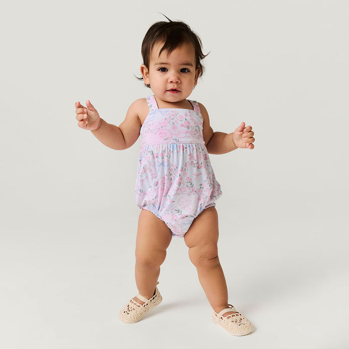 Baby wearing a pink floral romper on a plain background