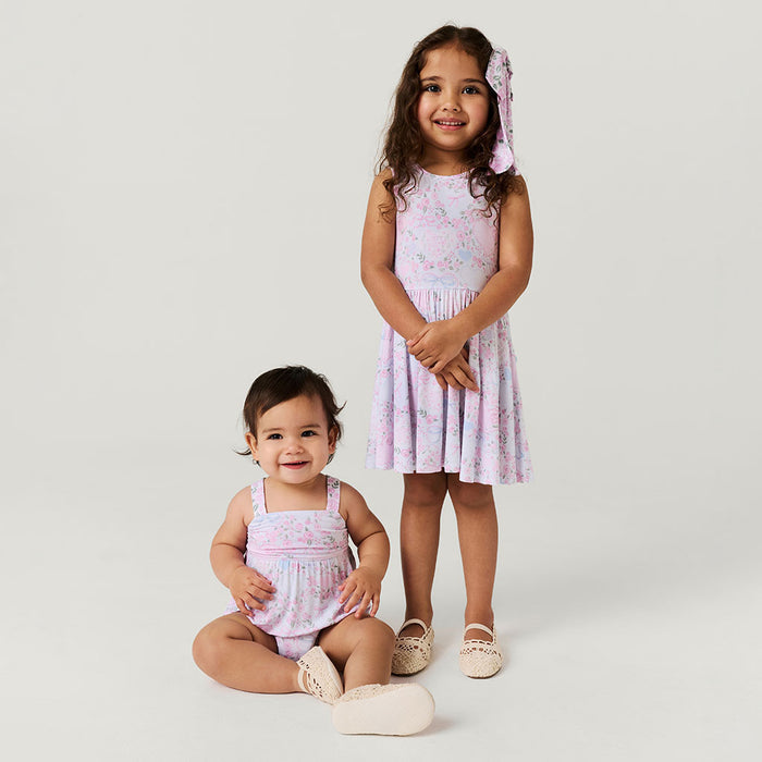 Two young girls wearing matching pink floral romper and dress on a white background