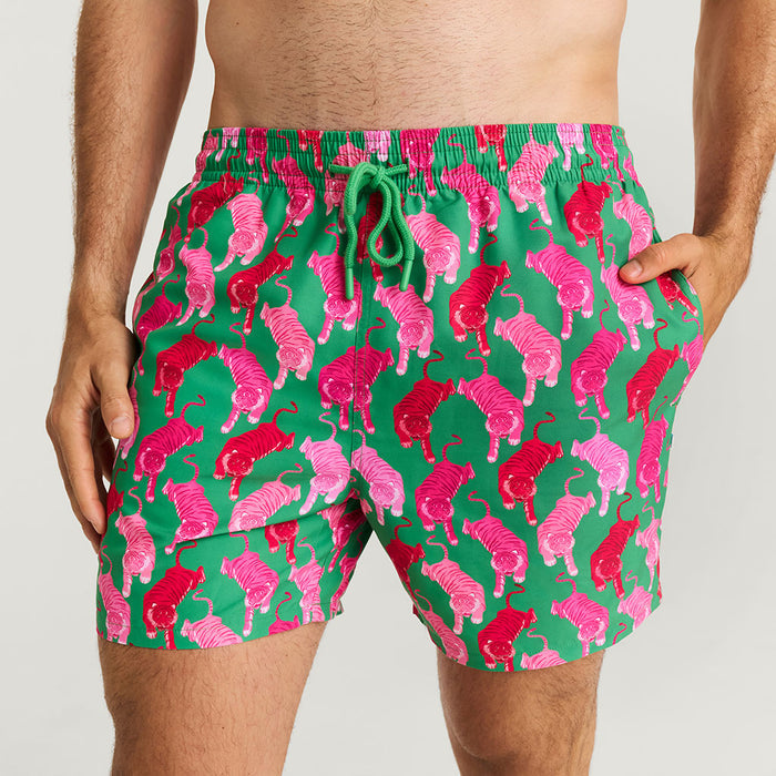 Green swim shorts with pink tiger pattern worn by a person on a white background