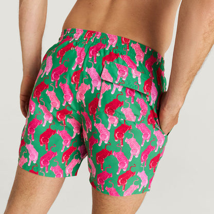 Green swim shorts with pink animal pattern worn by a person on a white background