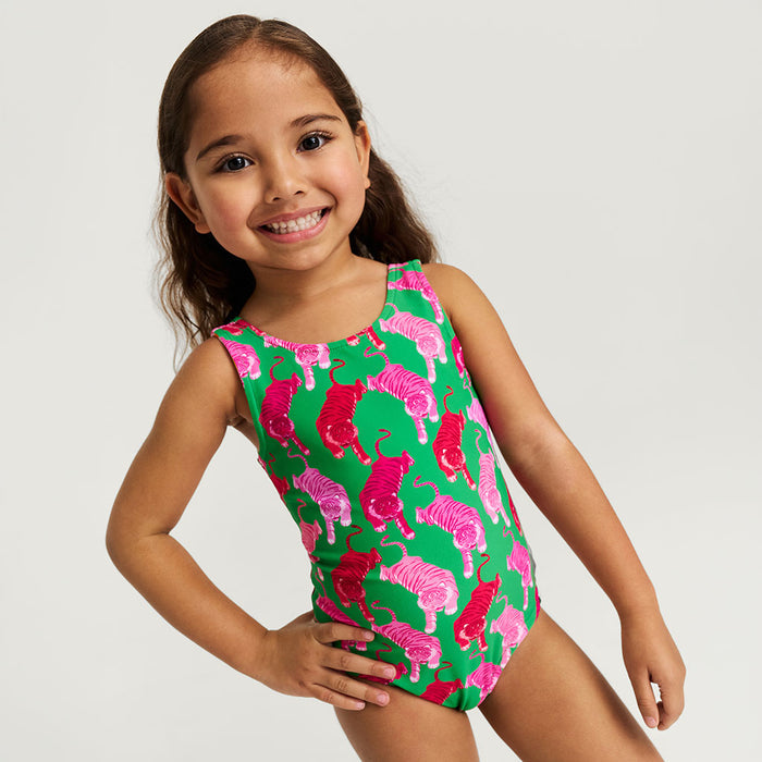Young girl wearing a colorful reversible swimsuit with pink and green design on a plain background