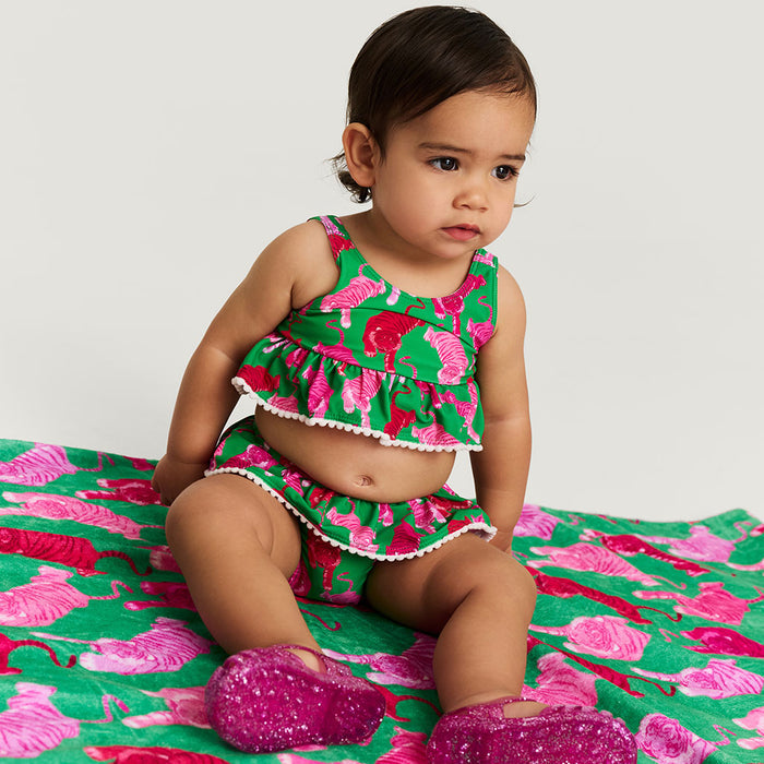 Child wearing a green and pink swimsuit outfit sitting on a matching fabric background.