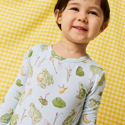 Close up of young boy  wearing blue bamboo viscose pajama set with frog prince print standing in front of a yellow checkered background.