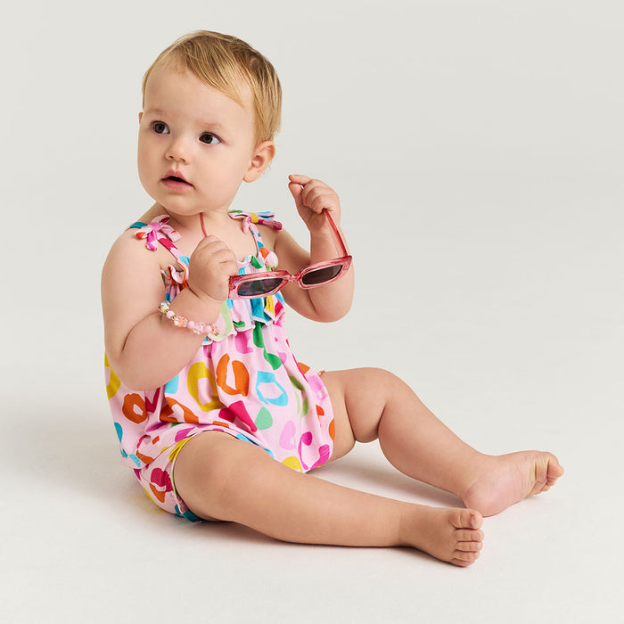 Baby wearing a colorful leopard print set and sunglasses on a plain background