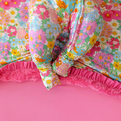 Colorful floral quilt with pink ruffled edge on a pink background