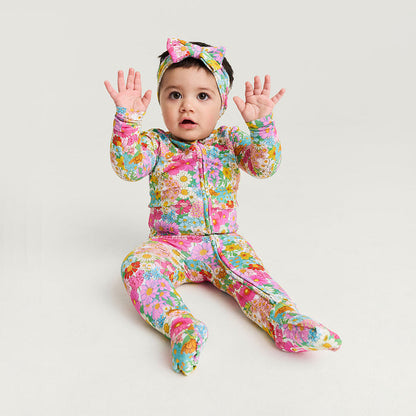 Baby in a colorful floral outfit with a headband on a light gray background