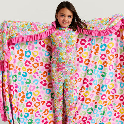 Child wearing a colorful outfit with a floral and leopard print pattern, standing in front of a matching pink and multicolor patterned blanket.