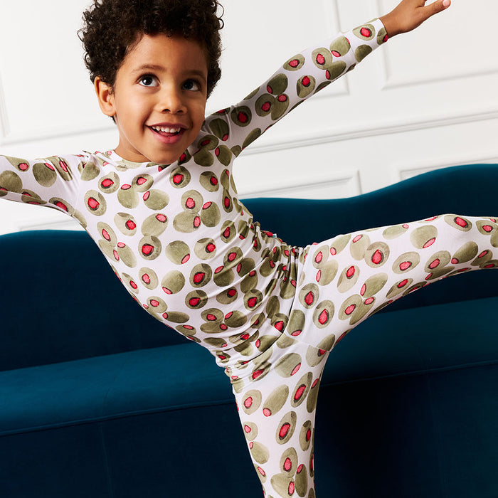 Child wearing a olive printed pajama set with arms outstretched on a blue couch.