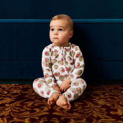 Baby wearing a olive patterned onesie sitting on a textured surface with a dark blue wall in the background
