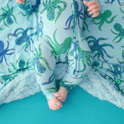 Baby in a onesie with octopus pattern in a crib with matching bedding.