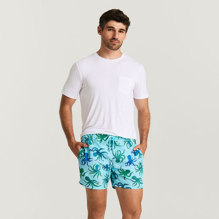 Man wearing a white t-shirt and blue shorts with octopus pattern on a light gray background