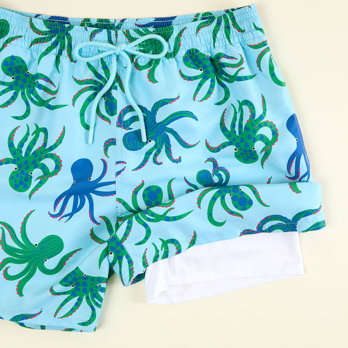 Blue swim shorts with green octopus pattern on a beige background