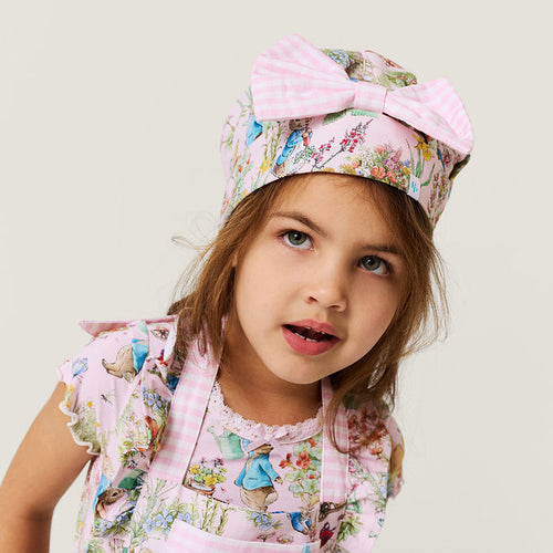 Young girl wearing a floral apron and matching chef's hat with a large bow on a light background