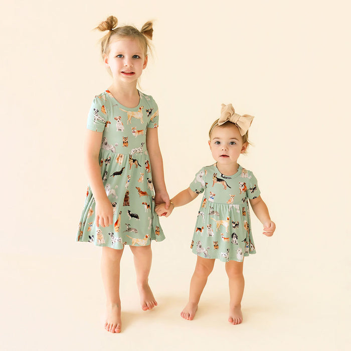 Two young girls wearing matching green dresses with animal prints on a beige background