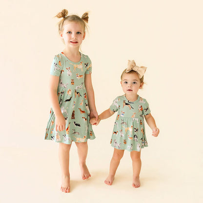 Two young girls wearing matching green dresses with animal prints on a beige background