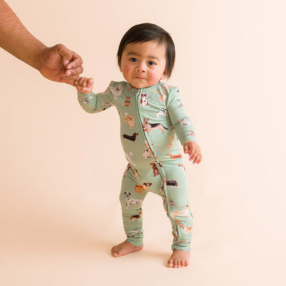 Child standing wearing a green one piece with dog patterned print.
