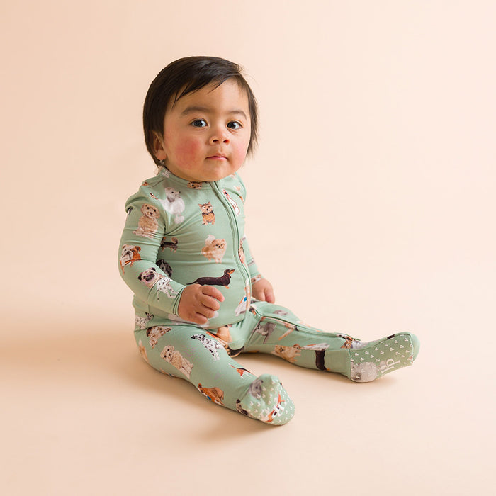 Child sitting wearing a green dog printed one piece on a beige background.