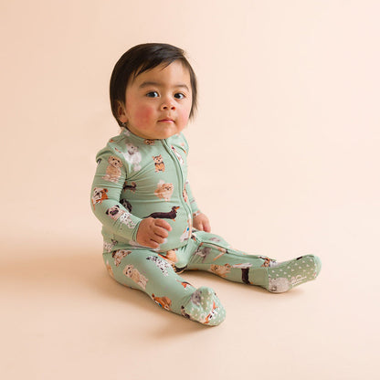 Child sitting wearing a green dog printed one piece on a beige background.
