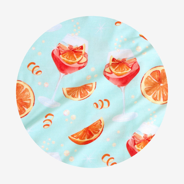 Round fabric swatch with aperol spritz cocktail-themed design on a light blue background