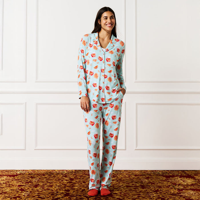 Woman wearing a aperol spritz cocktail pajama set against a white paneled wall.