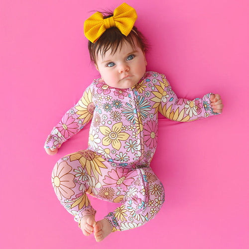 Baby in a floral outfit with a yellow bow on a pink background