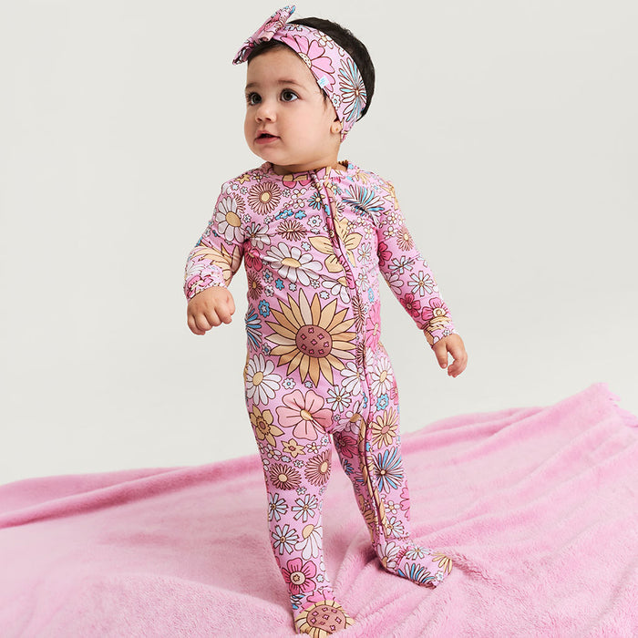 Baby in a floral onesie and headband on a pink blanket