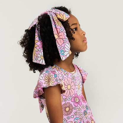 Young girl wearing a pink floral hair bow and dress against a light gray background