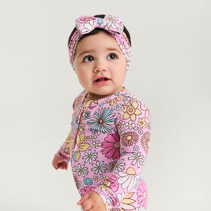 Baby wearing a floral pink outfit with a matching headband on a light gray background