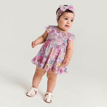 Baby wearing a pink floral dress and headband on a white background