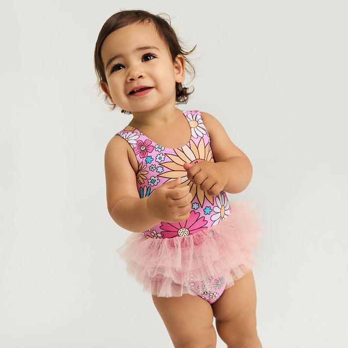 Child wearing a pink floral swimsuit with a tutu on a light gray background