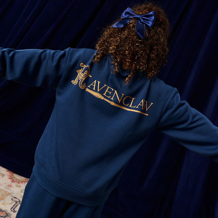 Child wearing a blue 'Ravenclaw' sweatshirt with gold lettering against a dark background.