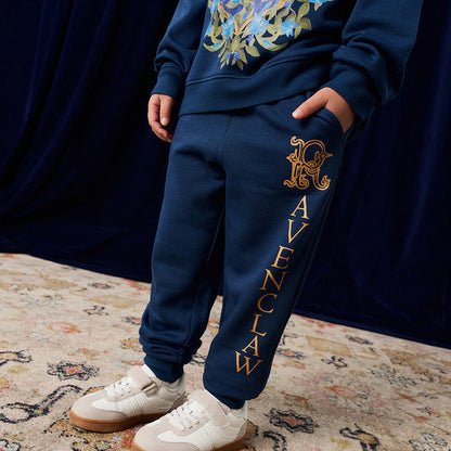 Child wearing navy jogger pant with 'Ravenclaw' text and logo, standing on a patterned rug.