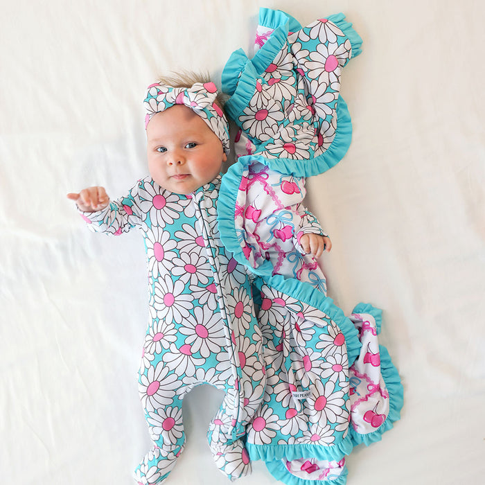 Baby in a floral outfit and hat lying on a white surface