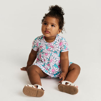 Child wearing a floral bodysuit dress sitting on a white background