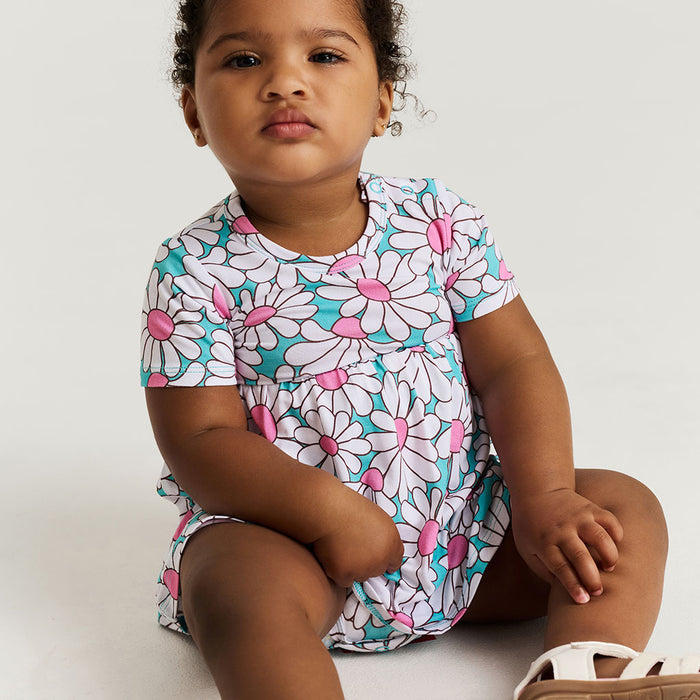 Child wearing a floral bodysuit dress sitting on a white background