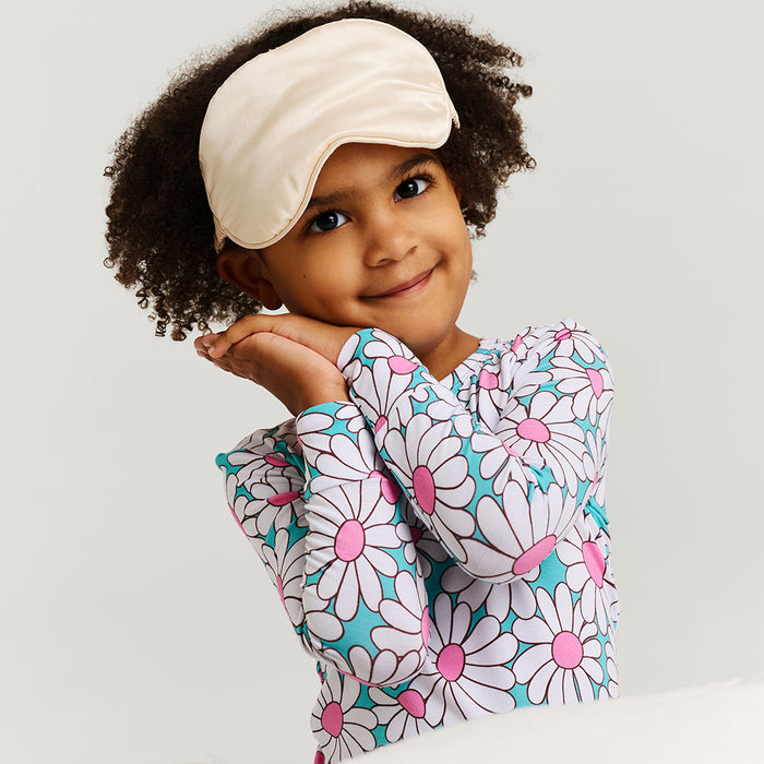 Child wearing a floral-patterned outfit with a white sleep mask on a light gray background