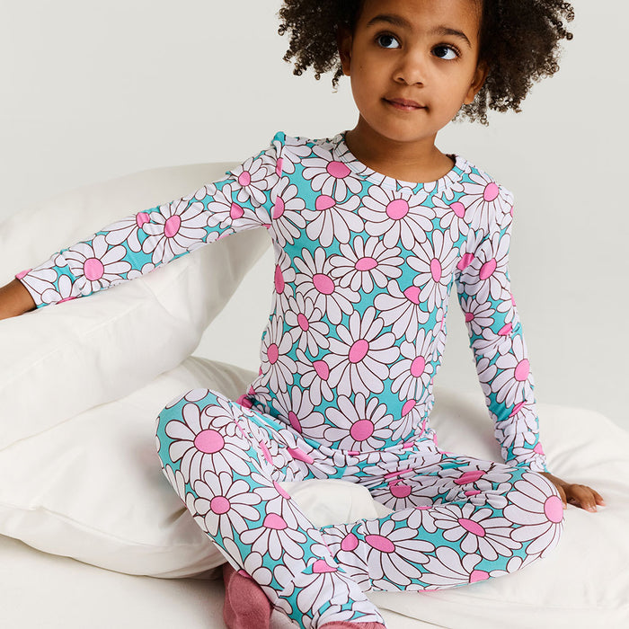 Child wearing a floral pajama set sitting on a bed.