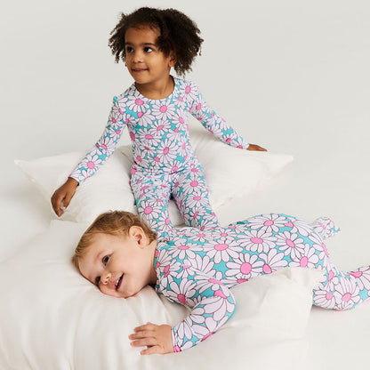 Two children wearing matching floral pajamas lying on a white bed.