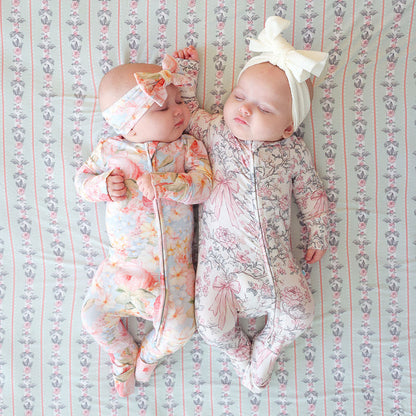 Two babies in floral outfits lying on a patterned blanket.
