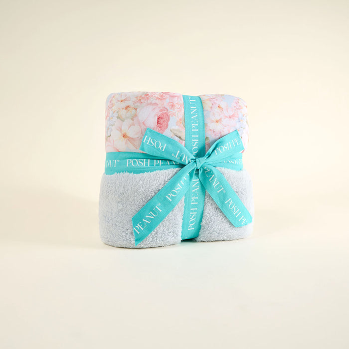 Folded blanket with floral pattern and turquoise ribbon on a light beige background