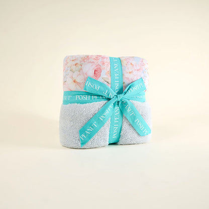Folded blanket with floral pattern and turquoise ribbon on a light beige background
