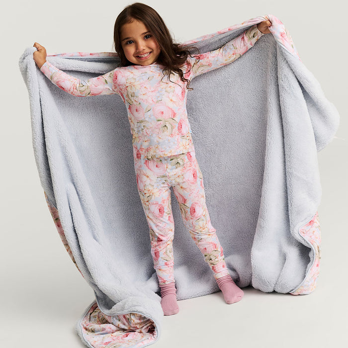 Child wearing a floral patterned pajama set holding a plush blanket over shoulders.