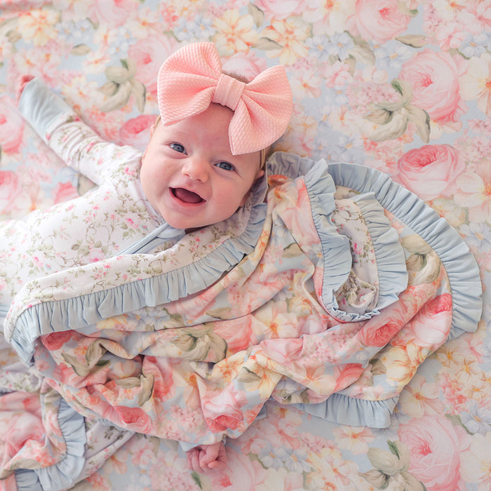 Baby wrapped in a floral blanket with a large pink bow on a floral background
