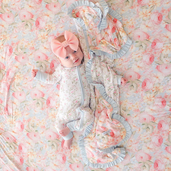 Baby lying on a floral blanket wearing a floral outfit with ruffles and a pink bow.